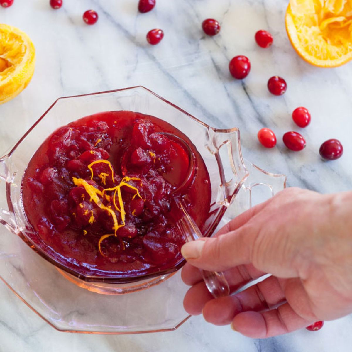 Woman's hand scooping cranberry orange sauce from a pink depression glass serving bowl.