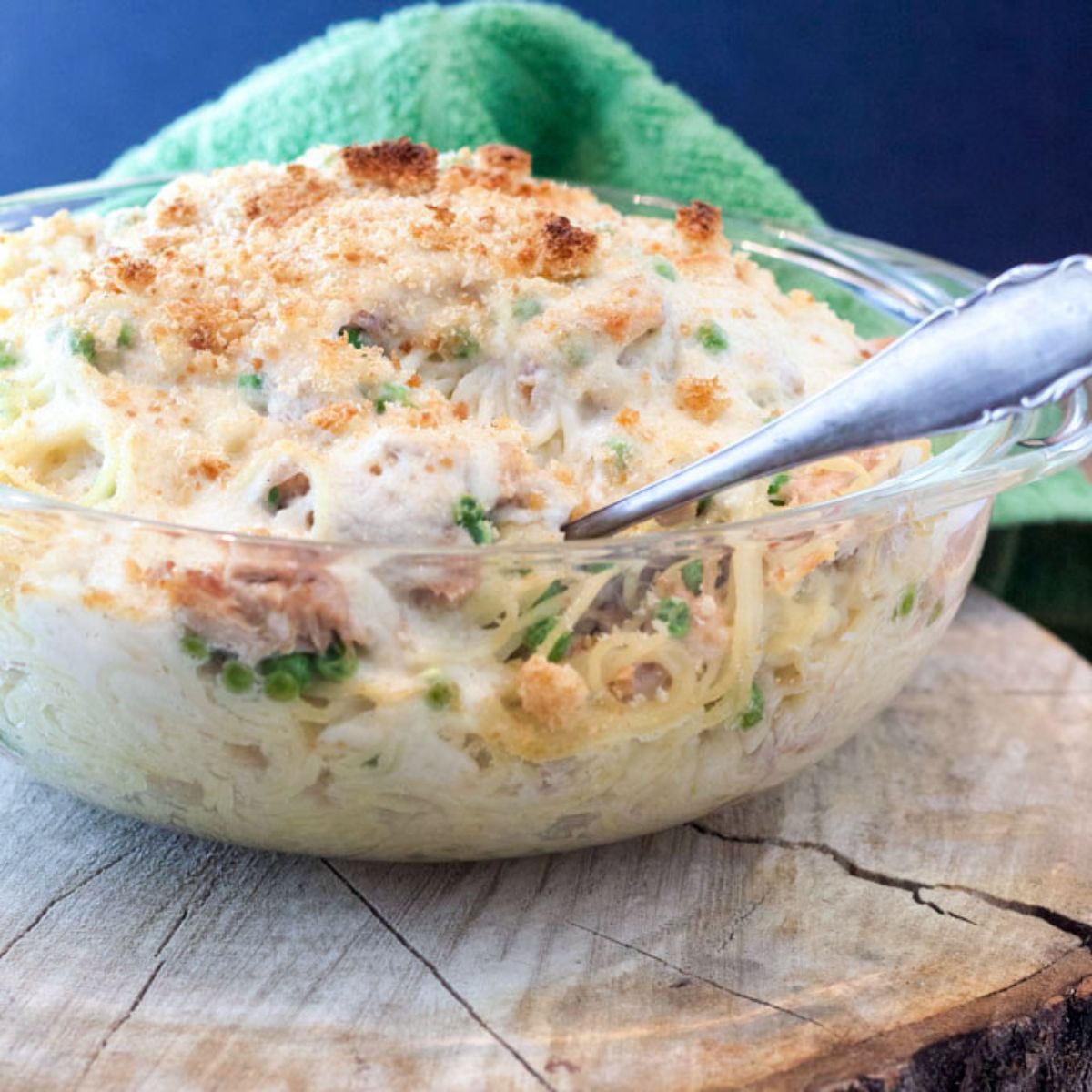 Heaping clear casserole dish with turkey spaghetti casserole with a creamy sauc and peas.