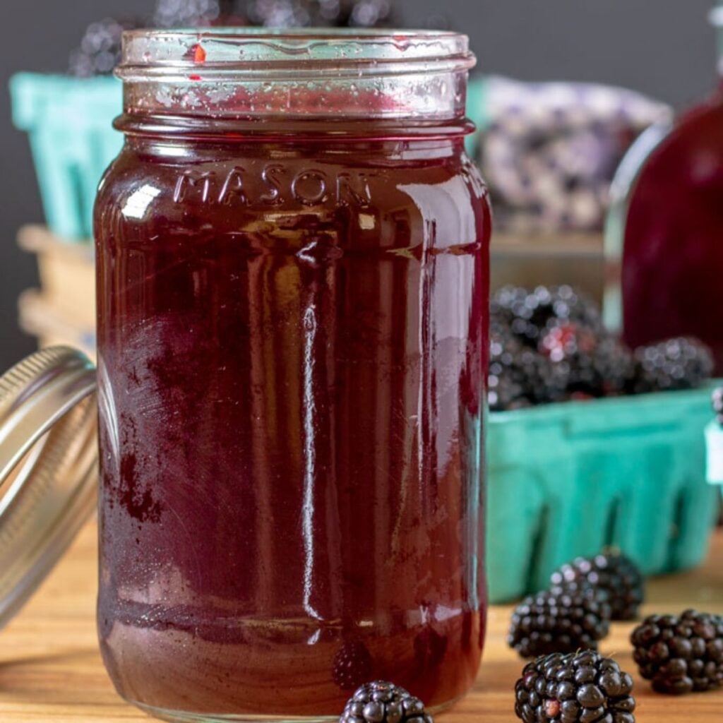 Jar of blackberry simple syrup with fresh blackberries in quart baskets.