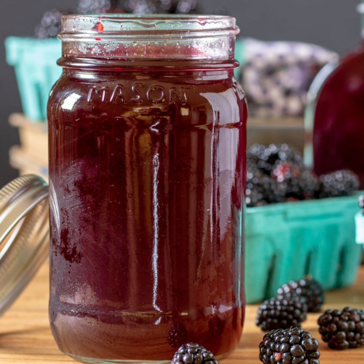 Jar of blackberry simple syrup with fresh blackberries in quart baskets.