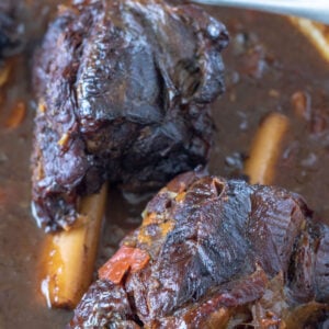 Close up of venison shanks in red wine sauce in Dutch oven.