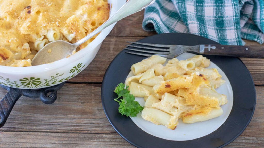 Classic mac & Cheese on white plate next to casserole dish.