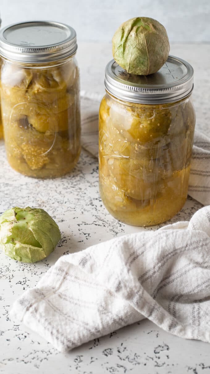 Jars of tomatillos with fresh tomatillo on top.