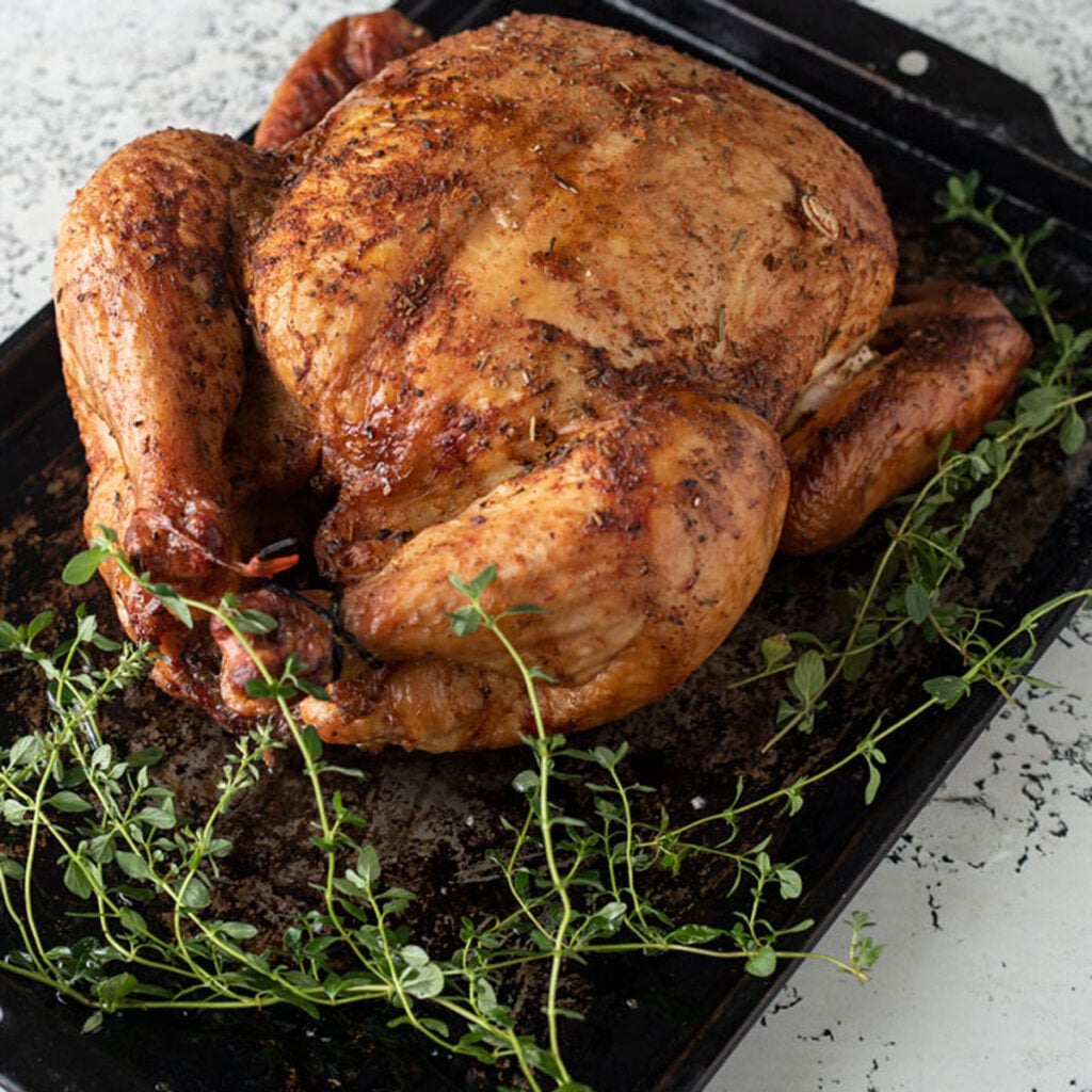 Whole browned chicken on a blackened metal tray.