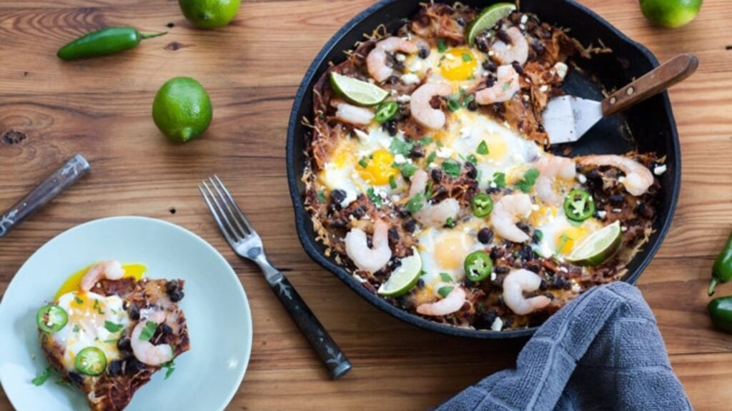 Small plate with chilaquiles next to cast iron skillet with shrimp chilaquiles.