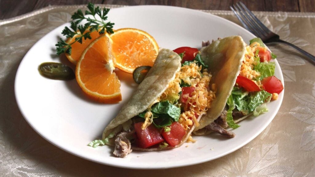 Pork tacos with slices of oranges on the side.
