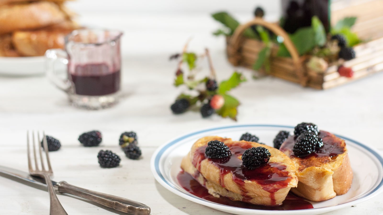 White plate with french toast topped with blackberry syrup and fresh blackberries