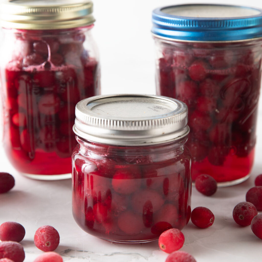 Jars of whole cranberries with cranberries on the board.