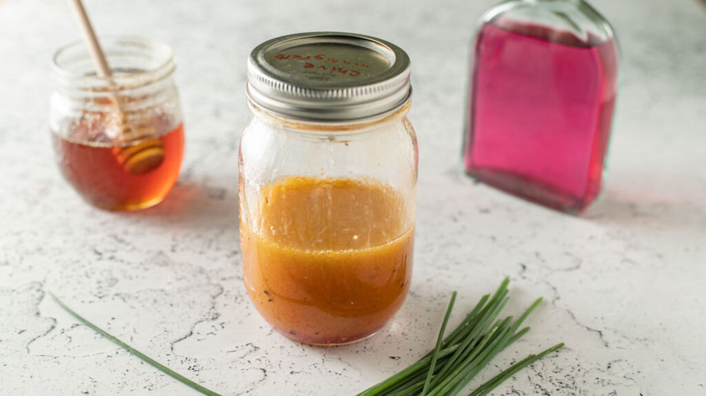 Jar with colorful chive vinaigrette next to bottles of vinegar.