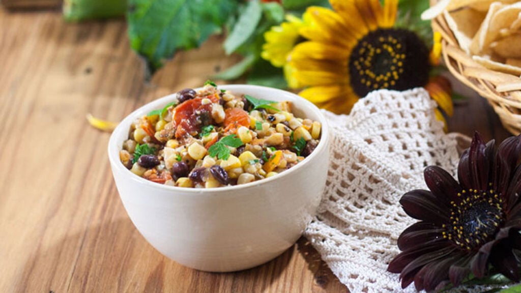 Roasted corn salsa in a small bowl, with fall flowers.