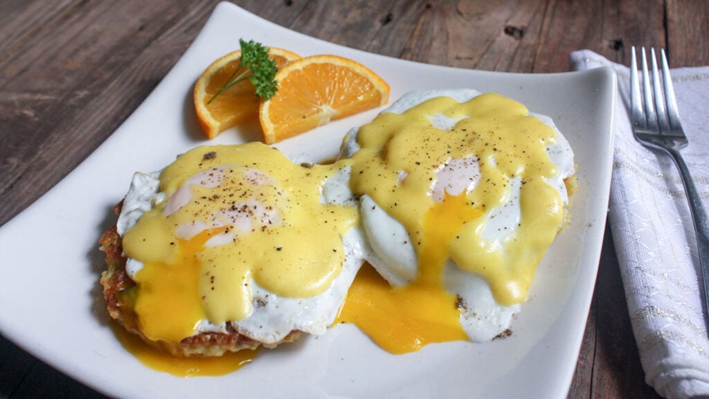 eggs benedict on white plate with broken yolks
