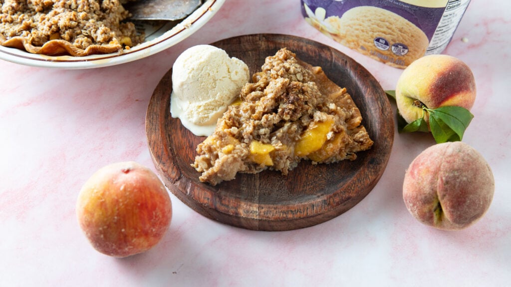 Slice of peach pie on a wooden plate.