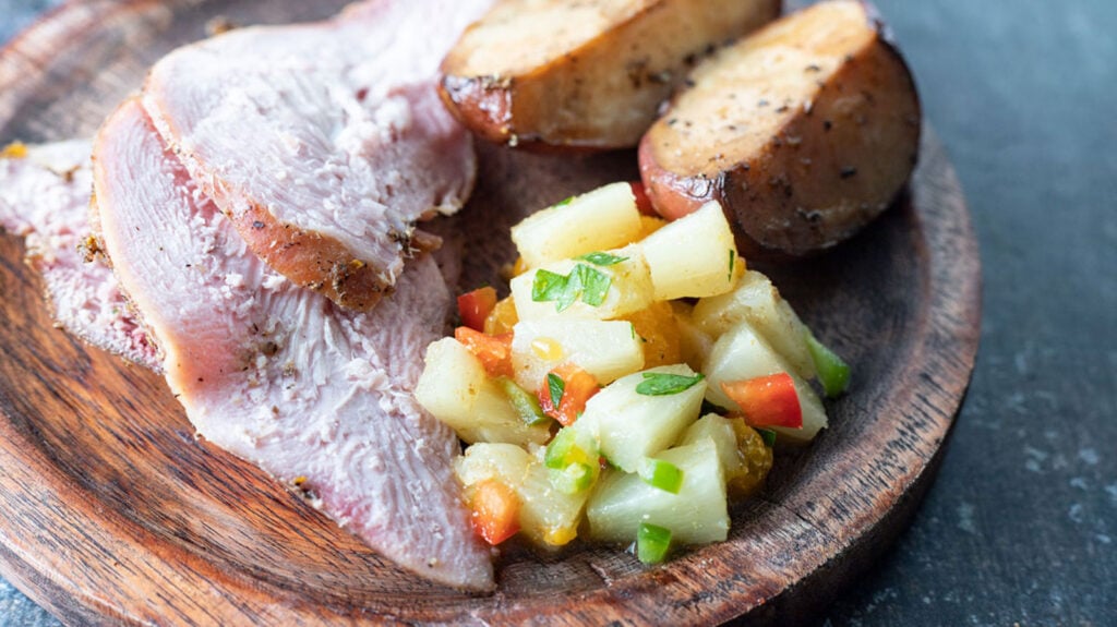 Sliced smoked pheasant on a wooden plate with sides.