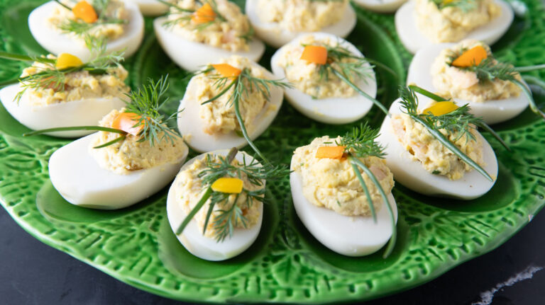 Green egg platter with colorful deviled eggs garnished with herbs.