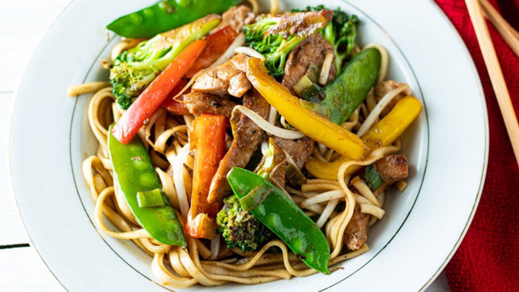 Close up of colorful chicken lo mein in a white bowl.