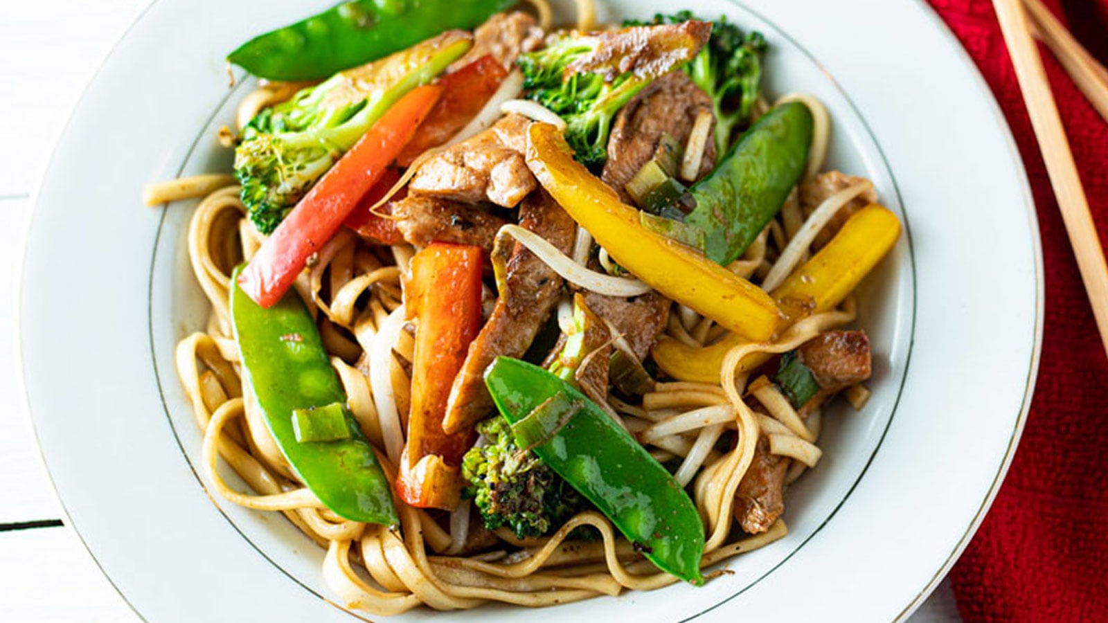 Close up of colorful chicken lo mein in a white bowl.