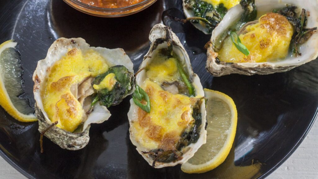 Oysters rockefeller on black plate.