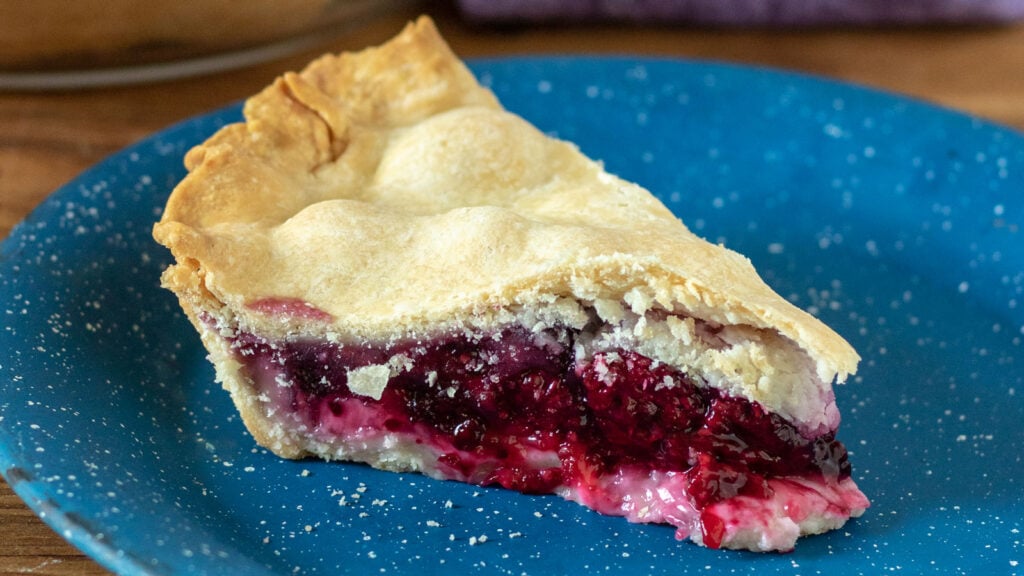 Slice of blackberry pie on a blue pewter plate.