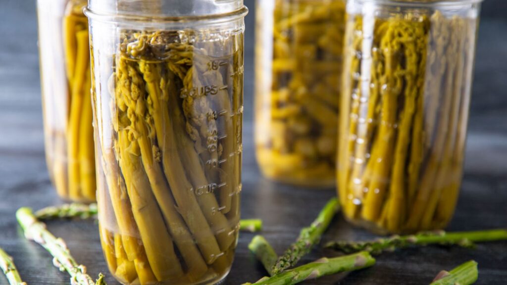 Jars of canned asparagus on a black board.