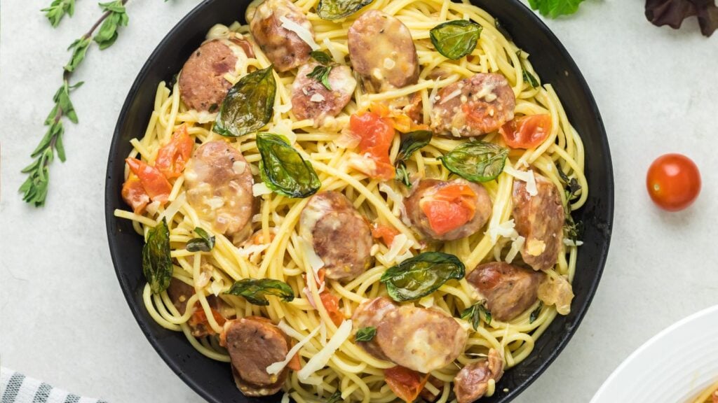 Large serving bowl with chorizo pasta with fried basil and fresh tomatoes.