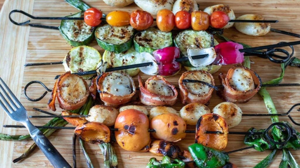 Skewered scallops and vegetables on a board.