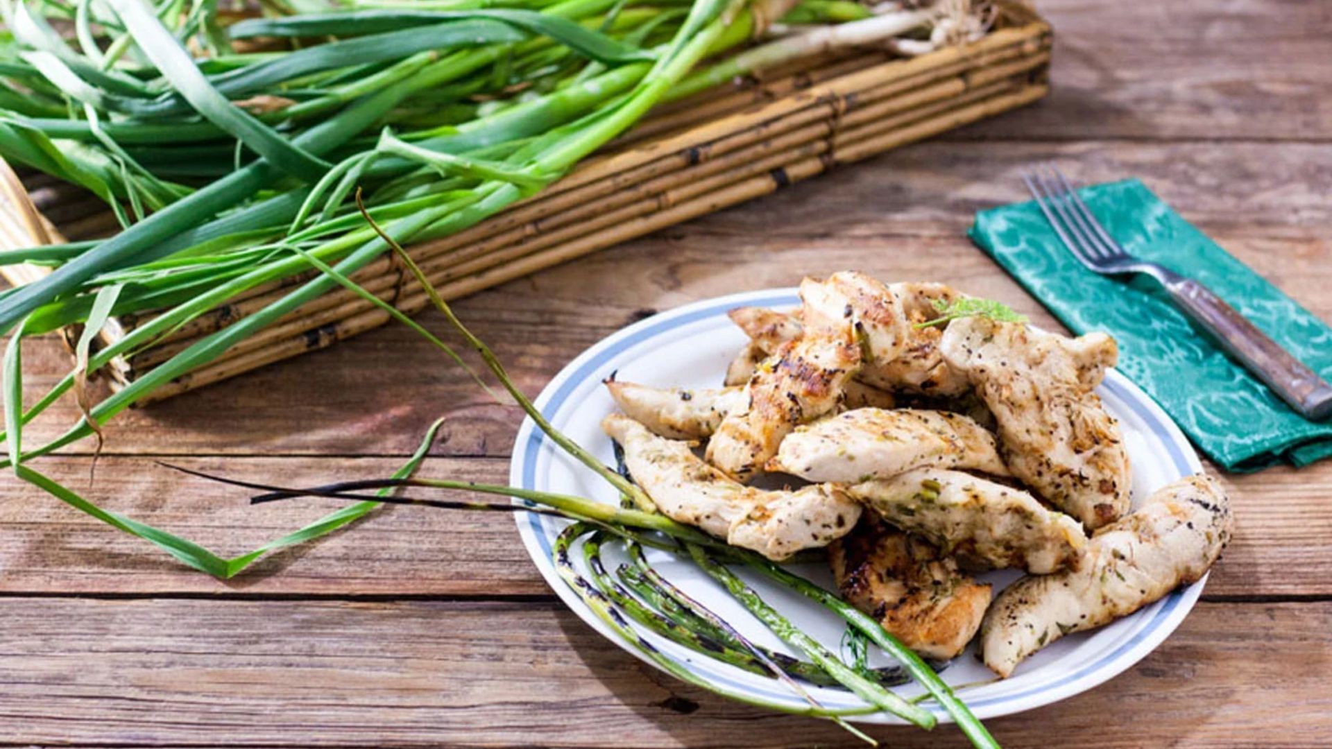 Chicken tenders piled on a plate with grilled garlic scapes.