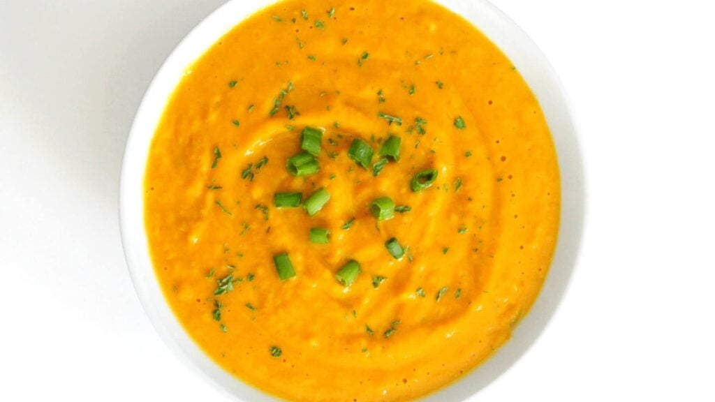 Pumpkin soup with chopped onion leaks on top.