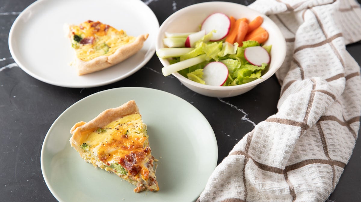 Slice of quiche on small plates with a little salad in a bowl.