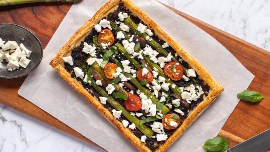Puff pastry with mushroom and asparagus on a wooden board.