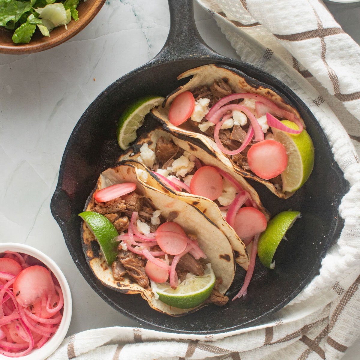 Black skillet with tacos and small bowls with toppings on the side.