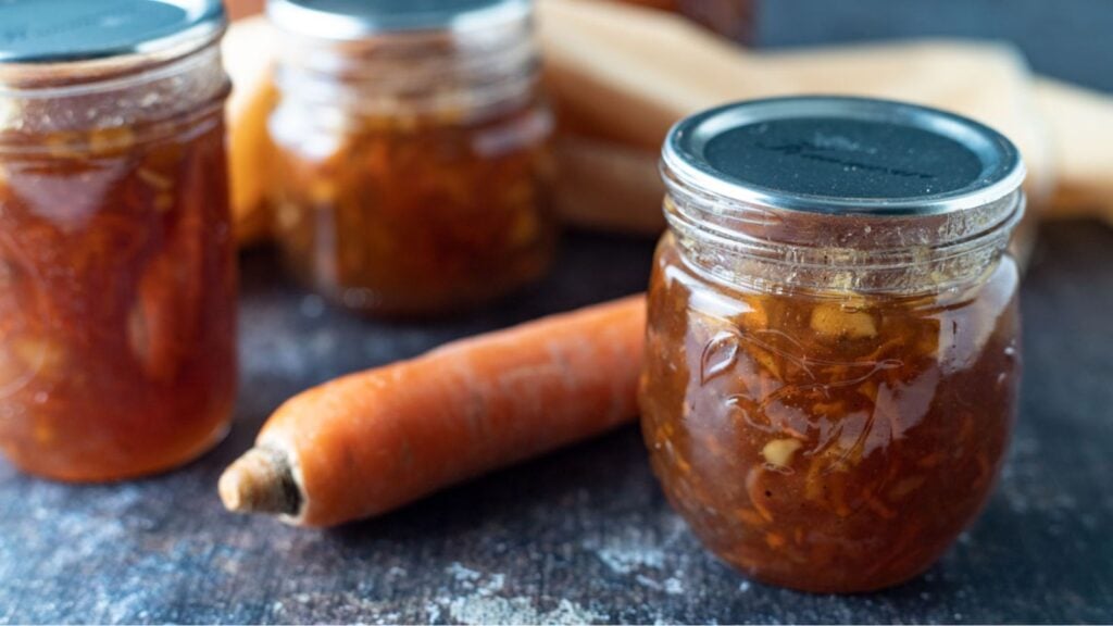 Jars of carrot cake jam with a raw carrot.