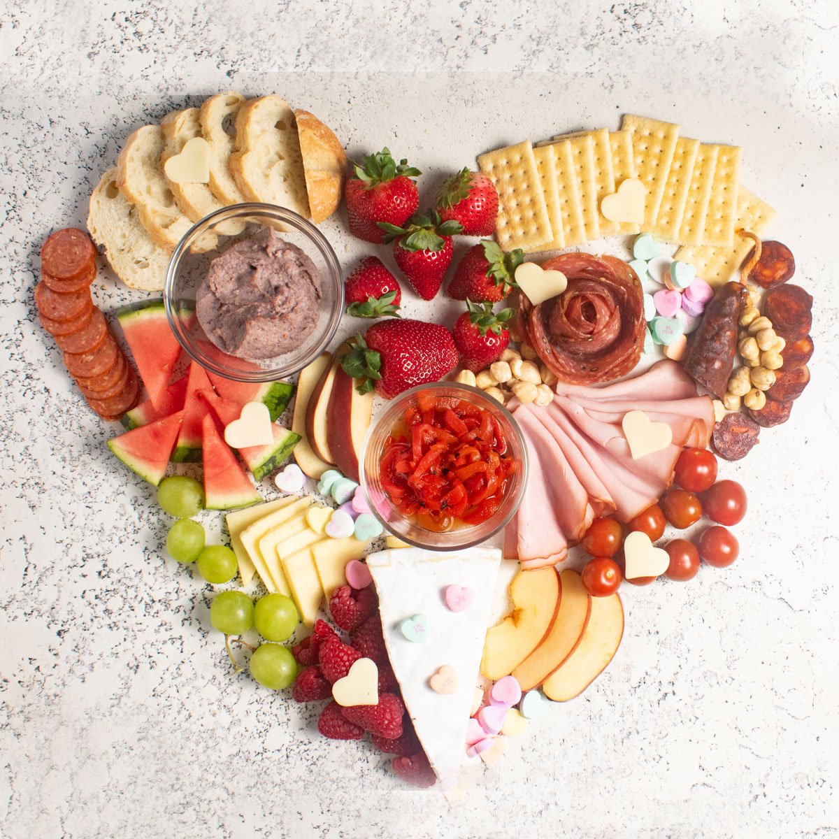 Heart-shaped Valentine's Charcuterie Board that is pink and w white.
