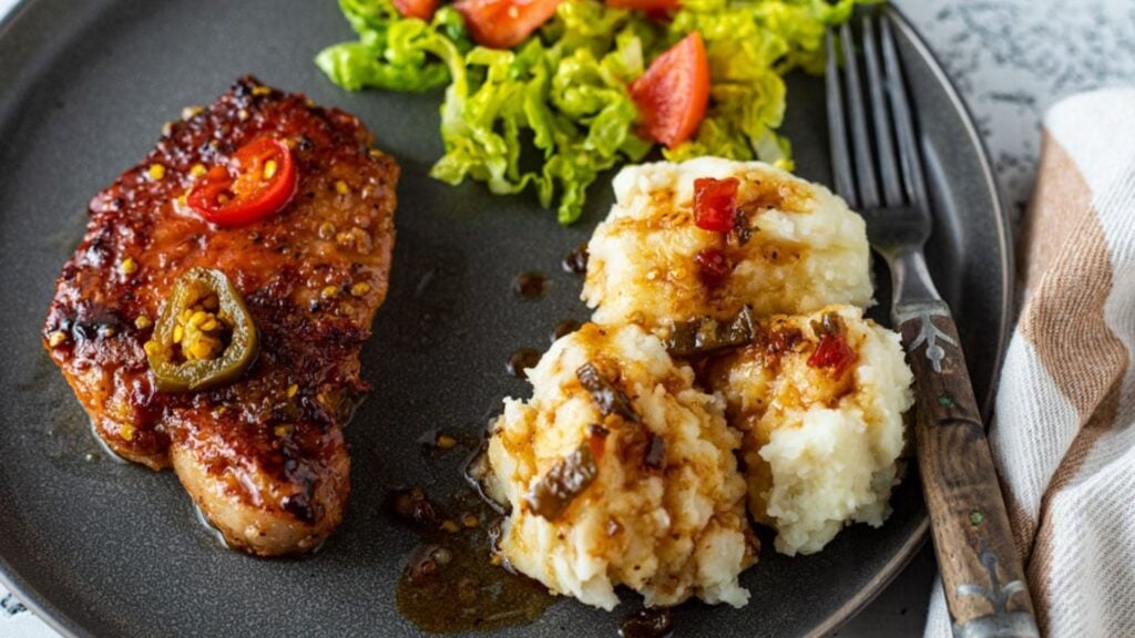 Pork chops on a black plate with side dishes.