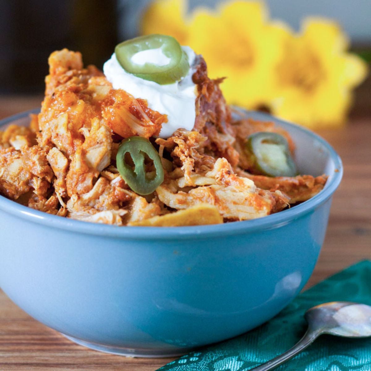 Chicken enchilada casserole in a blue bowl topped with sour cream and jalapenos.