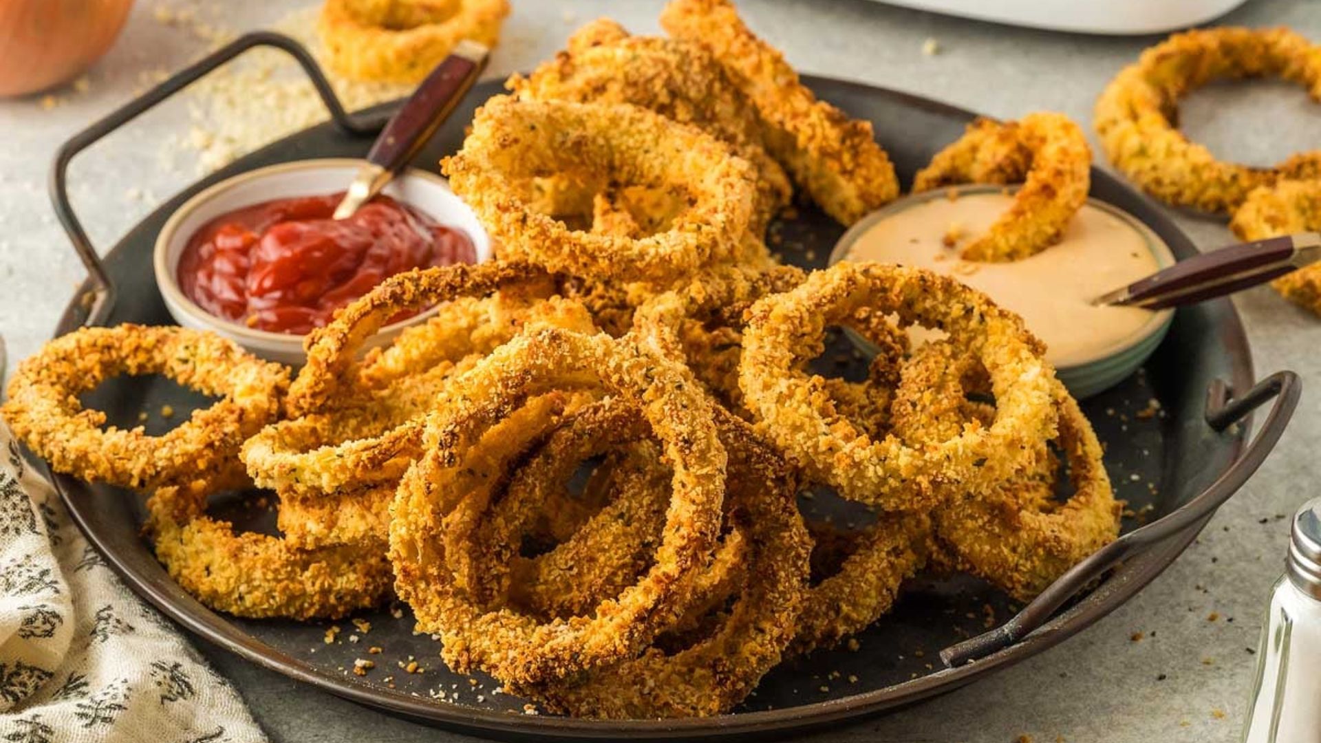 Air fryer onion rings with sauce on sides.