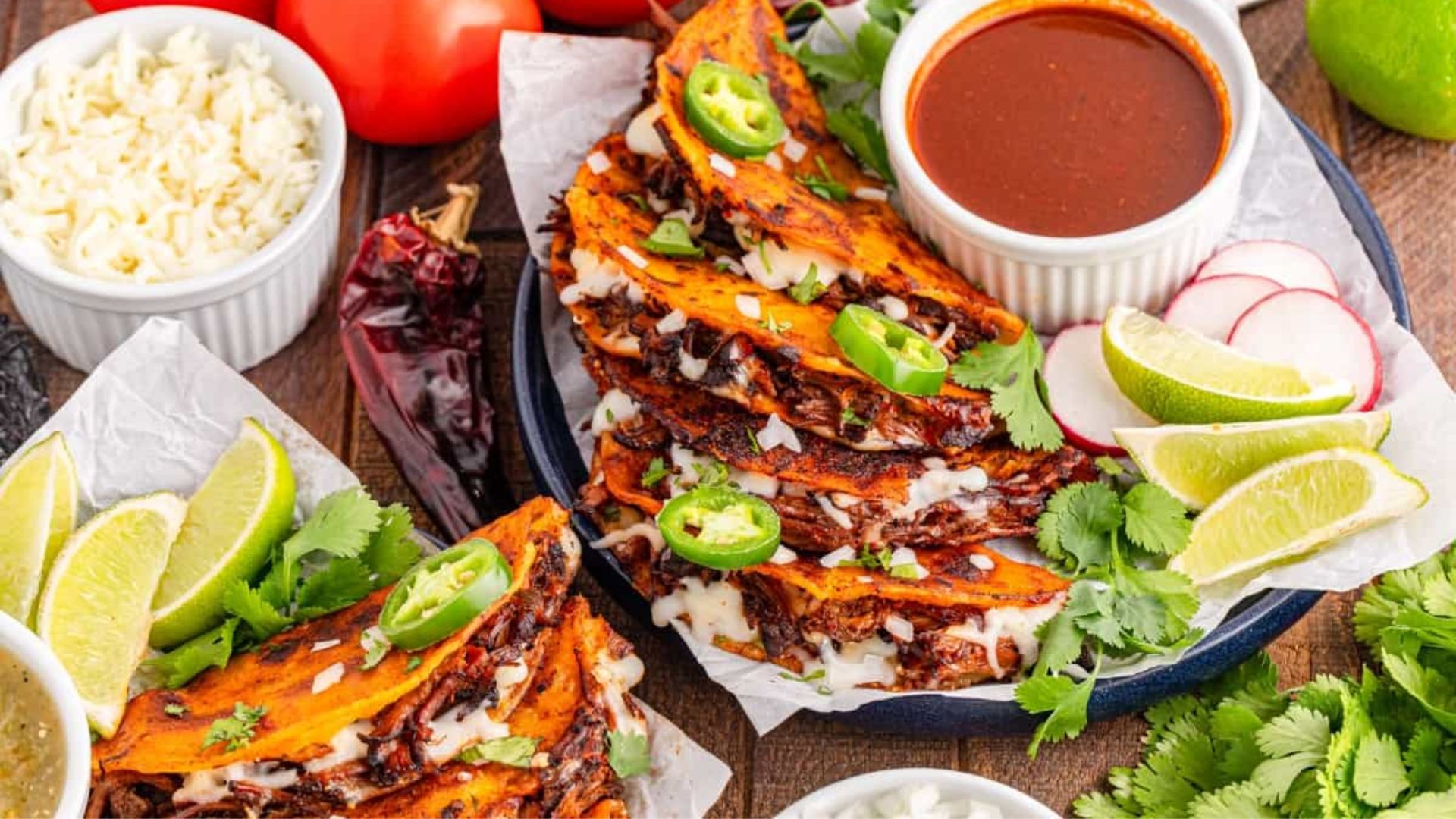 Quesabirria tacos with lime and herbs on side.