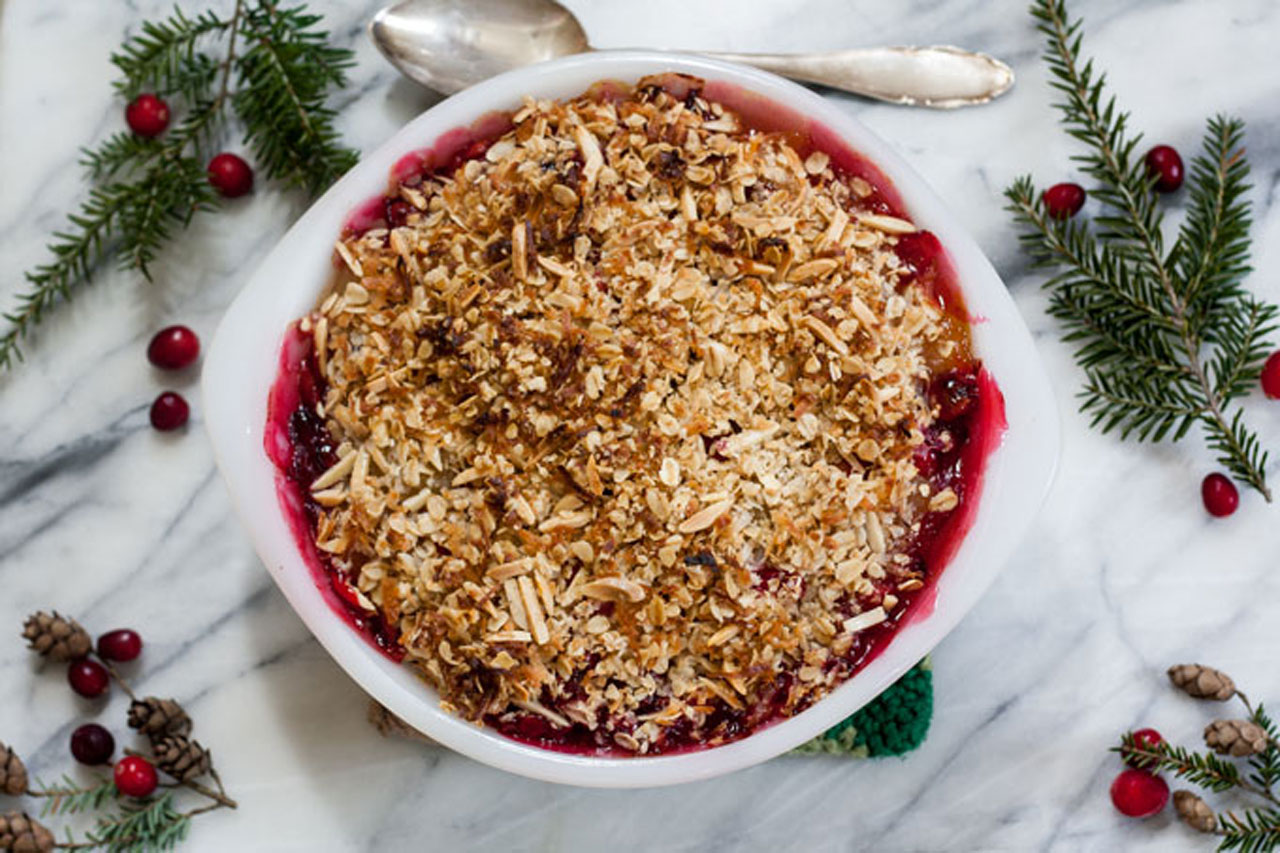 Overhead photo of apple cranberry crisp in a baking dish with a spoon and scattered cranberries.