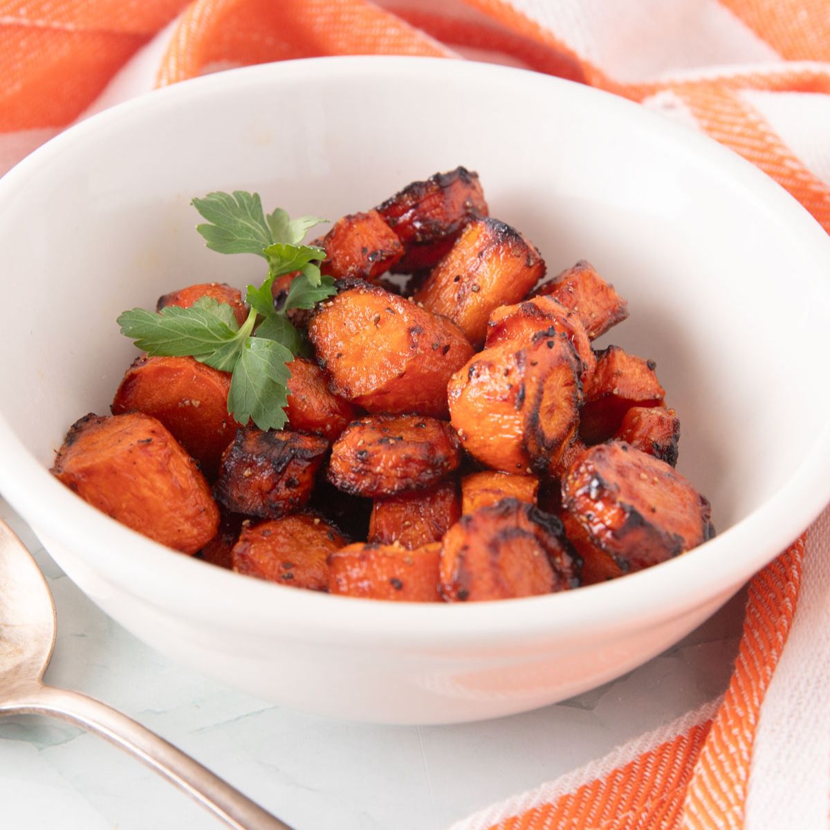 White bowl with golden roasted carrots garnished with fresh parsley.