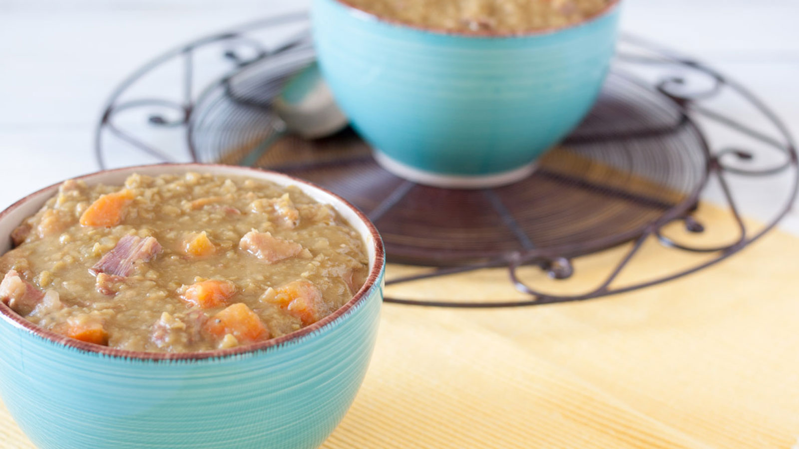Two green bowls of split pea soup loaded with ham and vegetables.