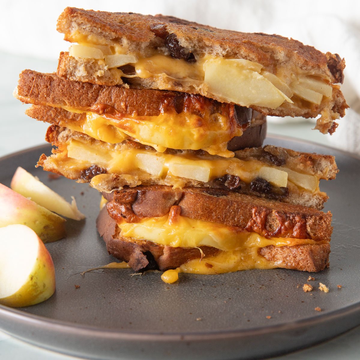 Four halved apple grilled cheese sandwiches stack on a gray plate with slices of apple on the side.