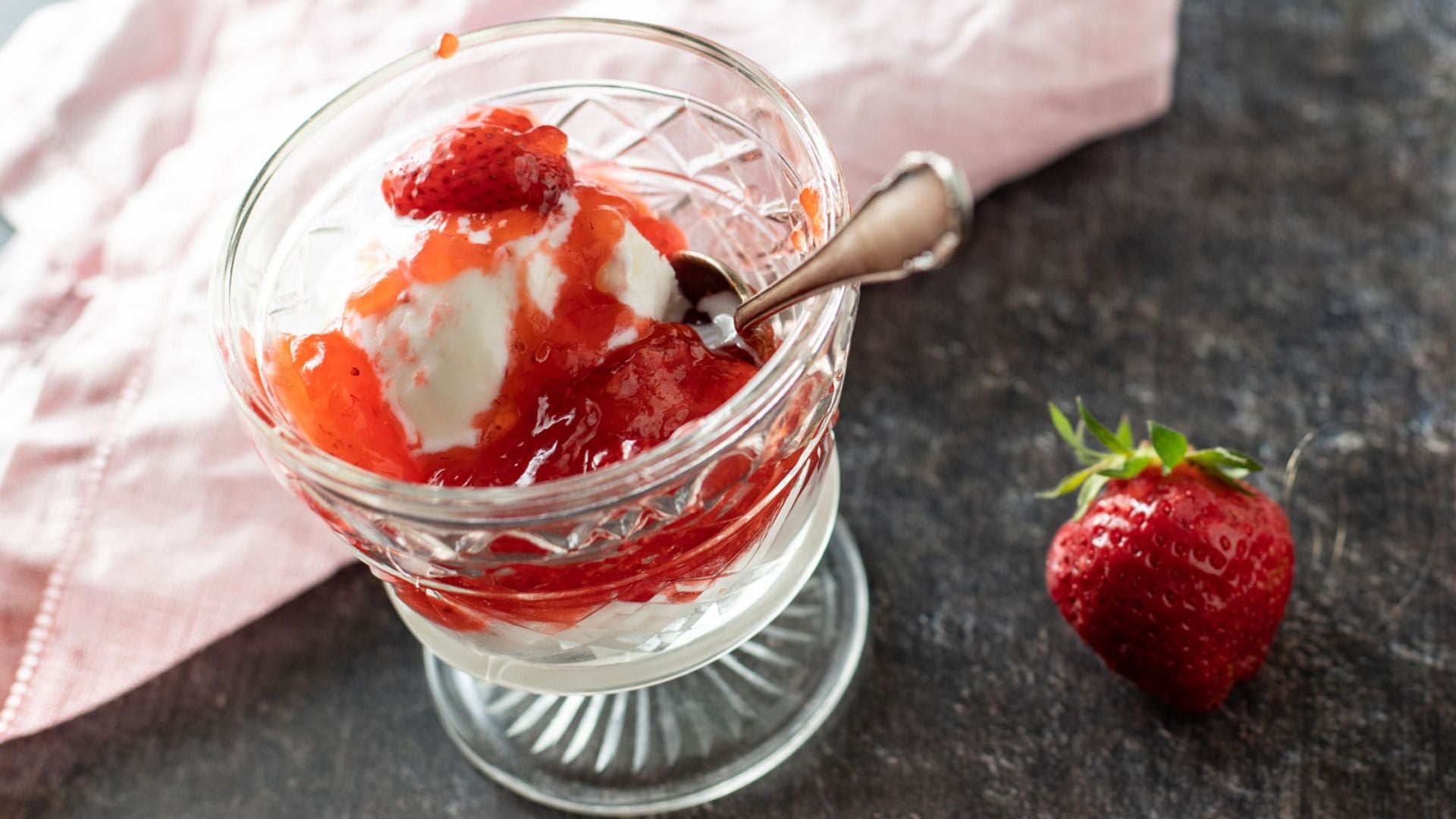Strawberry pie filling over ice cream in a glass.