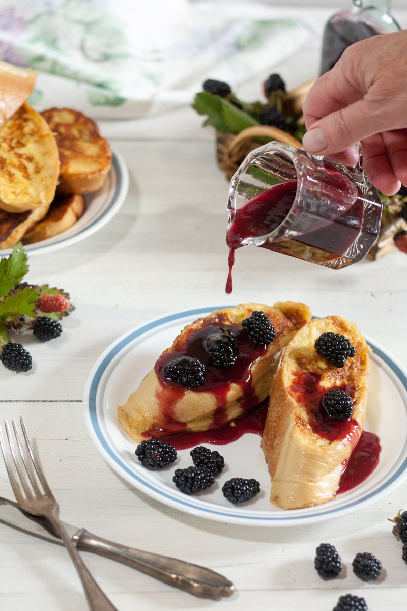 Hand pouring blackberry syrup onto French toast
