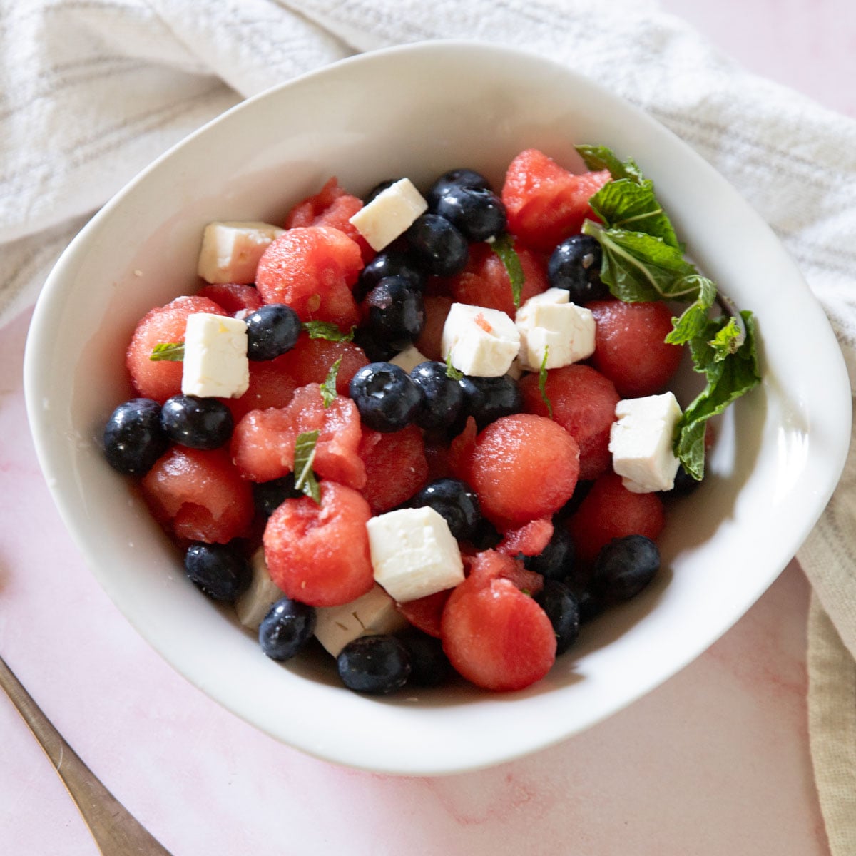 Red white and blue salad in a white bowl with a white kitchen towel.