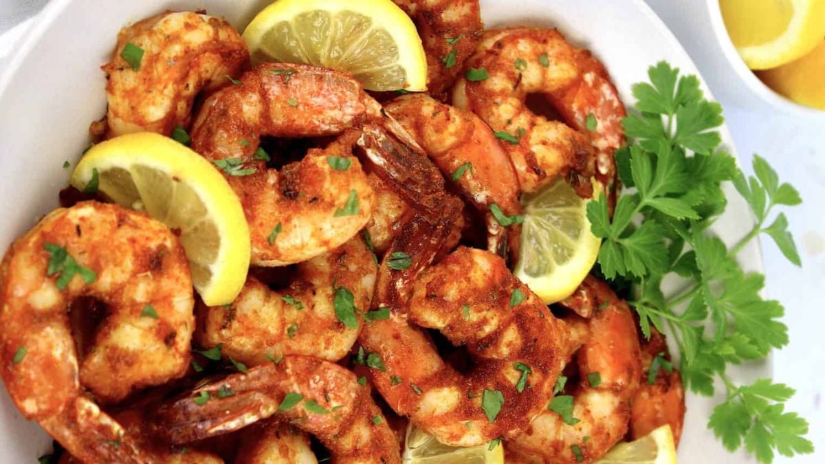 Air fryer blackened shrimp served with lemon wedges and garnished with fresh parsley on a white plate.