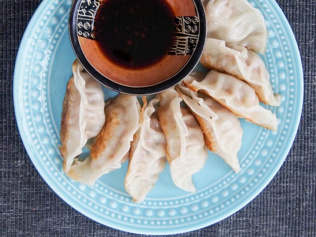 A plate of Chinese Pork And Cabbage Dumplings with soy sauce on the side