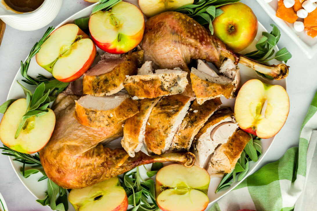 A platter of Apple Cider Baked Turkey with apples and leaves as garnish.