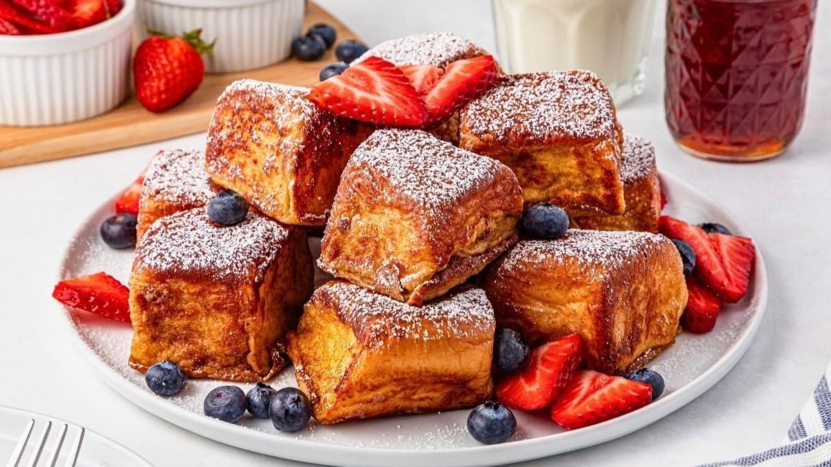 Cubed French toast with berries and powdered sugar on a plate.