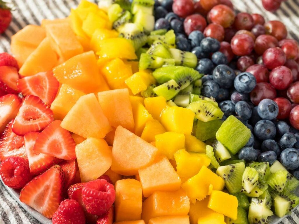 A close-up shot of different colored fruits arranged in the order of rainbow colors.