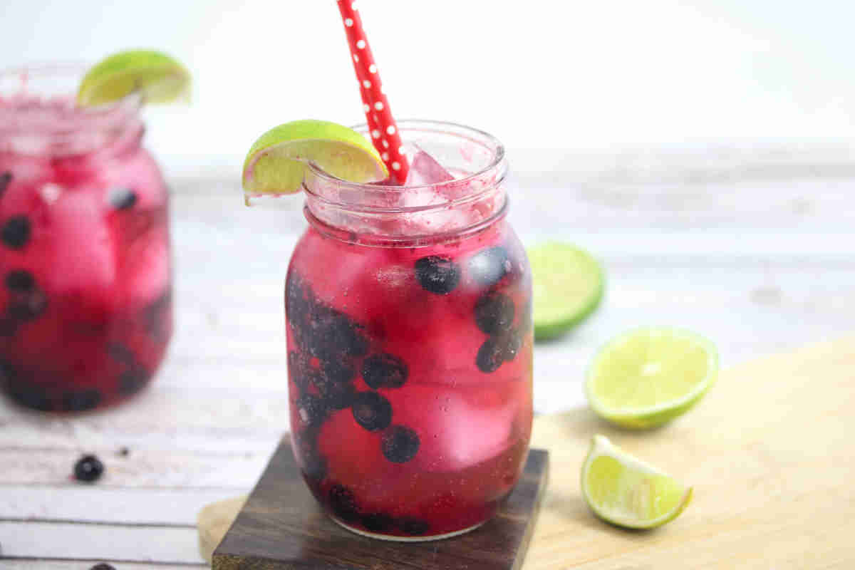 A glass of Sparkling Blueberry Mocktail with a straw and a polka-dotted straw.