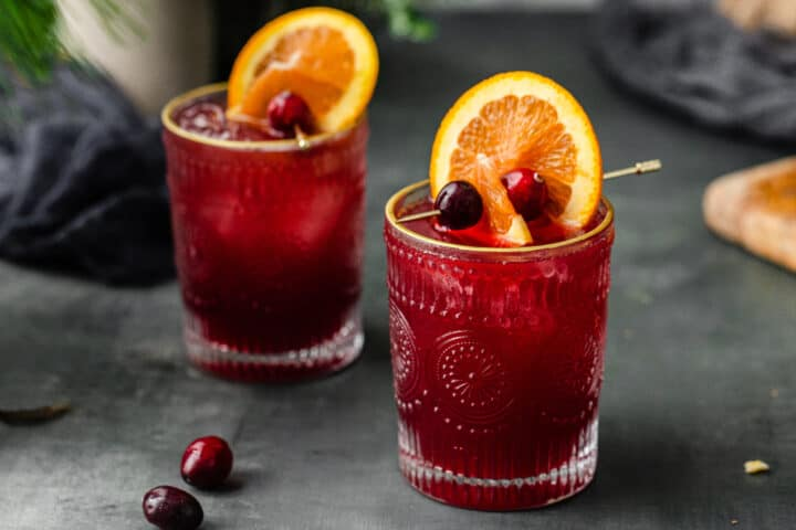 Two glasses of Cranberry and Orange Juice Mocktail with fruits garnished on top.